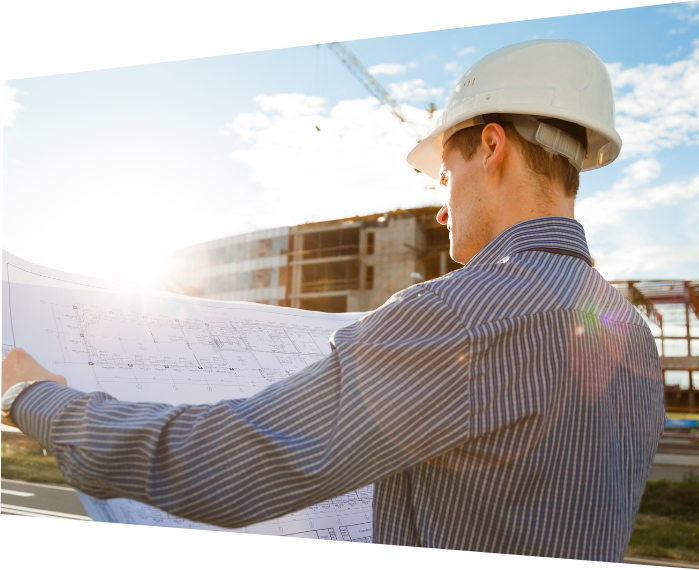 General Contracting: A view from behind the shoulder of a General Contractor reviewing blueprint sketches with a construction zone in the background. General Contracting: A view from behind the shoulder of a General Contractor reviewing blueprint sketches with a construction zone in the background.